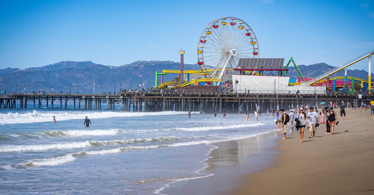 Scenic view of Santa Monica Pier with Ferris wheel, beach, and people enjoying a sunny day.